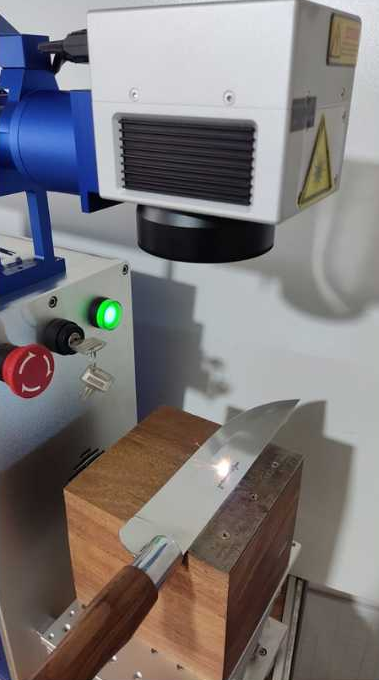 Máquina de laser de fibra gravando um logotipo na lâmina de uma faca Pazpazini